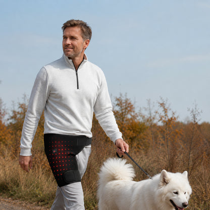 Man använder värmande LED-massageband för höft och lår med röd ljusterapi under promenad utomhus med hund.