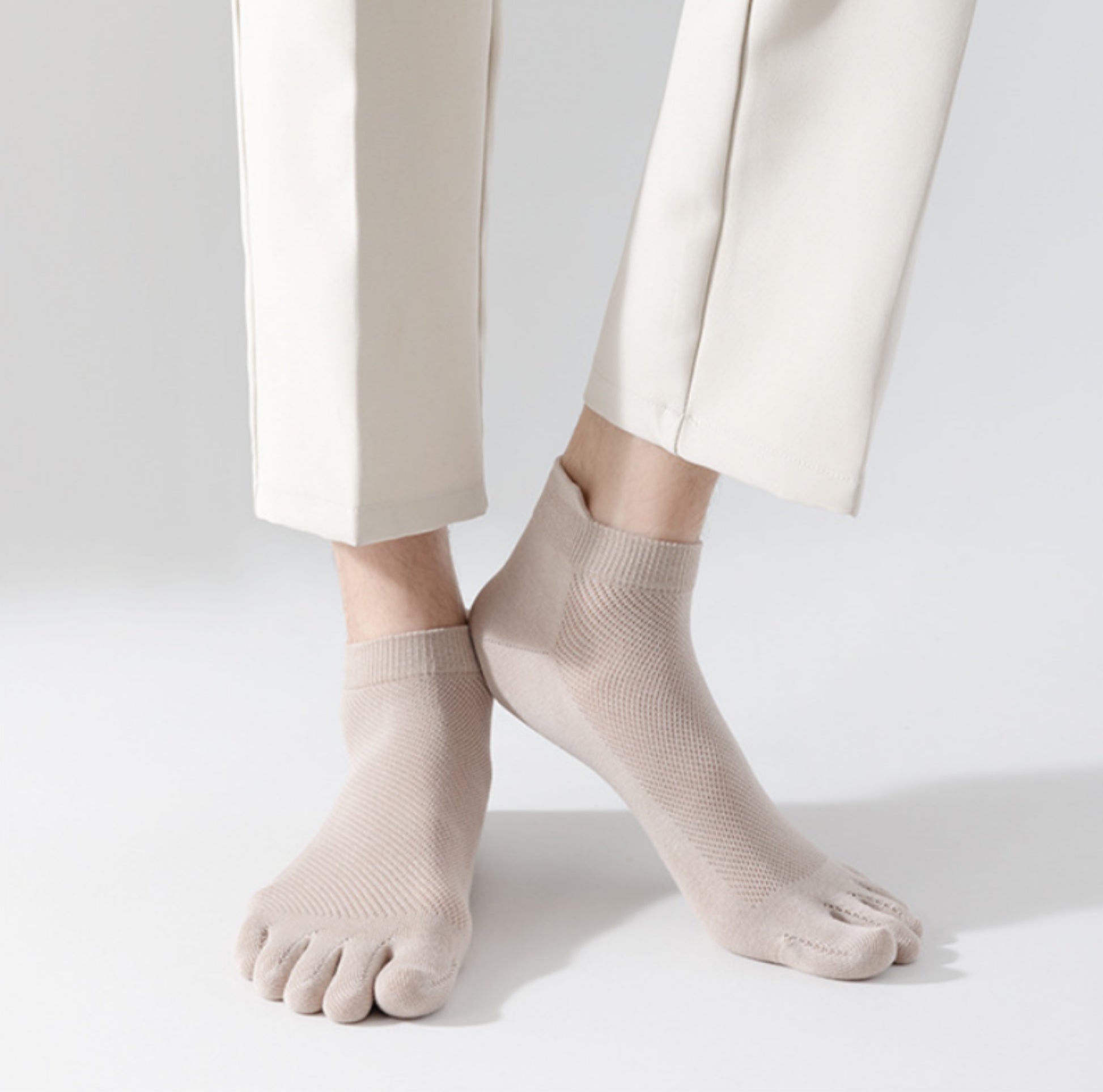 Person står på ljus bakgrund med tunna tåstrumpor i mjukt, följsamt material som separerar tårna och sitter tätt runt foten